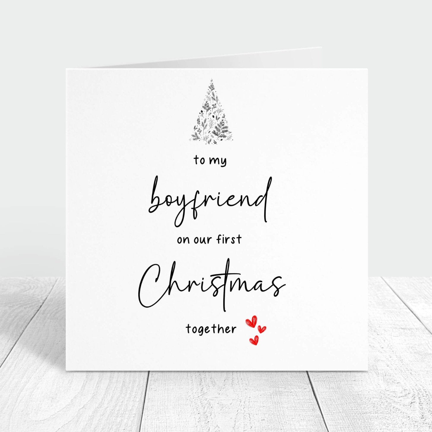 Personalised Christmas card for boyfriend with the message "To my boyfriend on our first Christmas together," featuring a festive tree and red hearts.