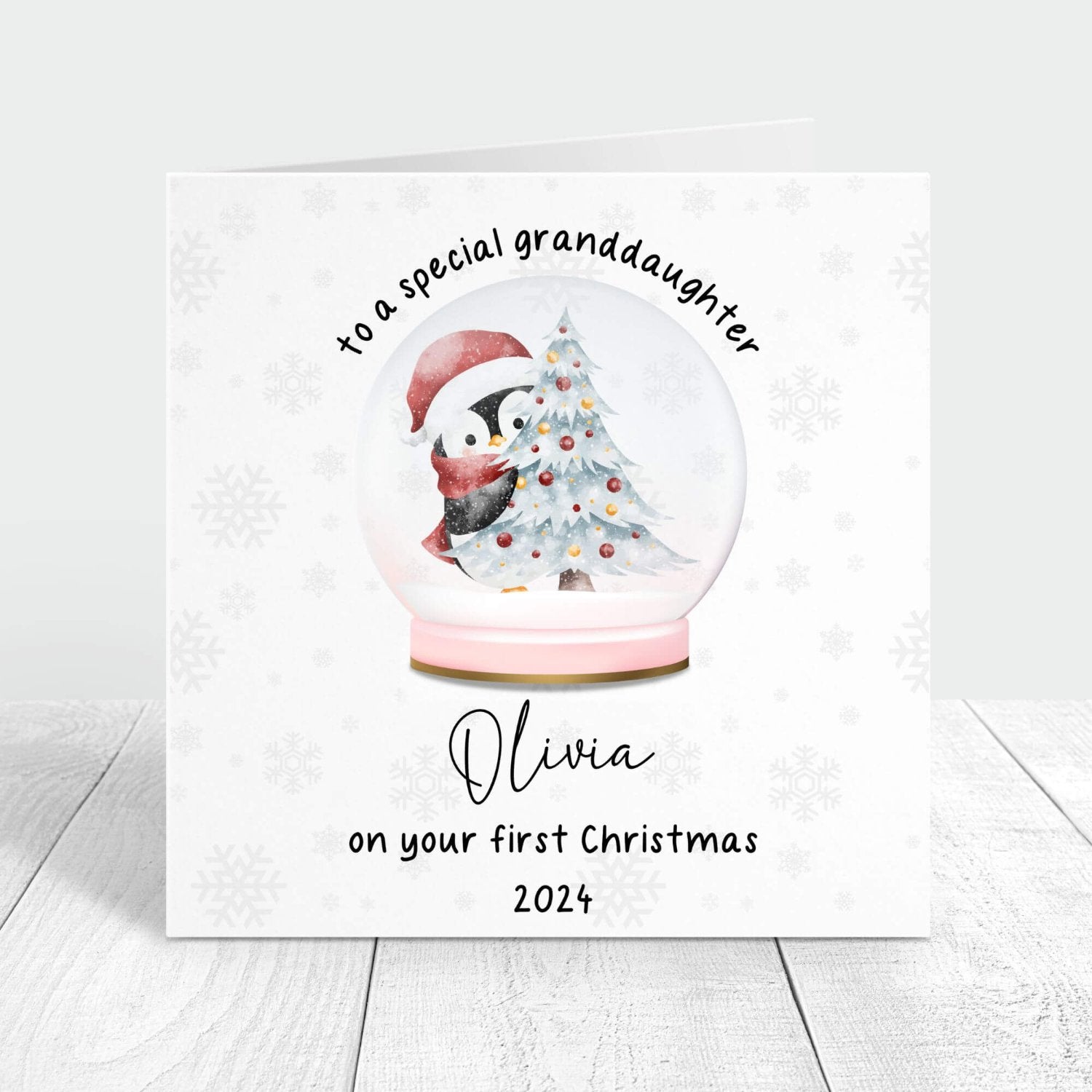 Personalised first Christmas card for granddaughter featuring a snow globe with a penguin and Christmas tree. Customised with her name and the year 2024.