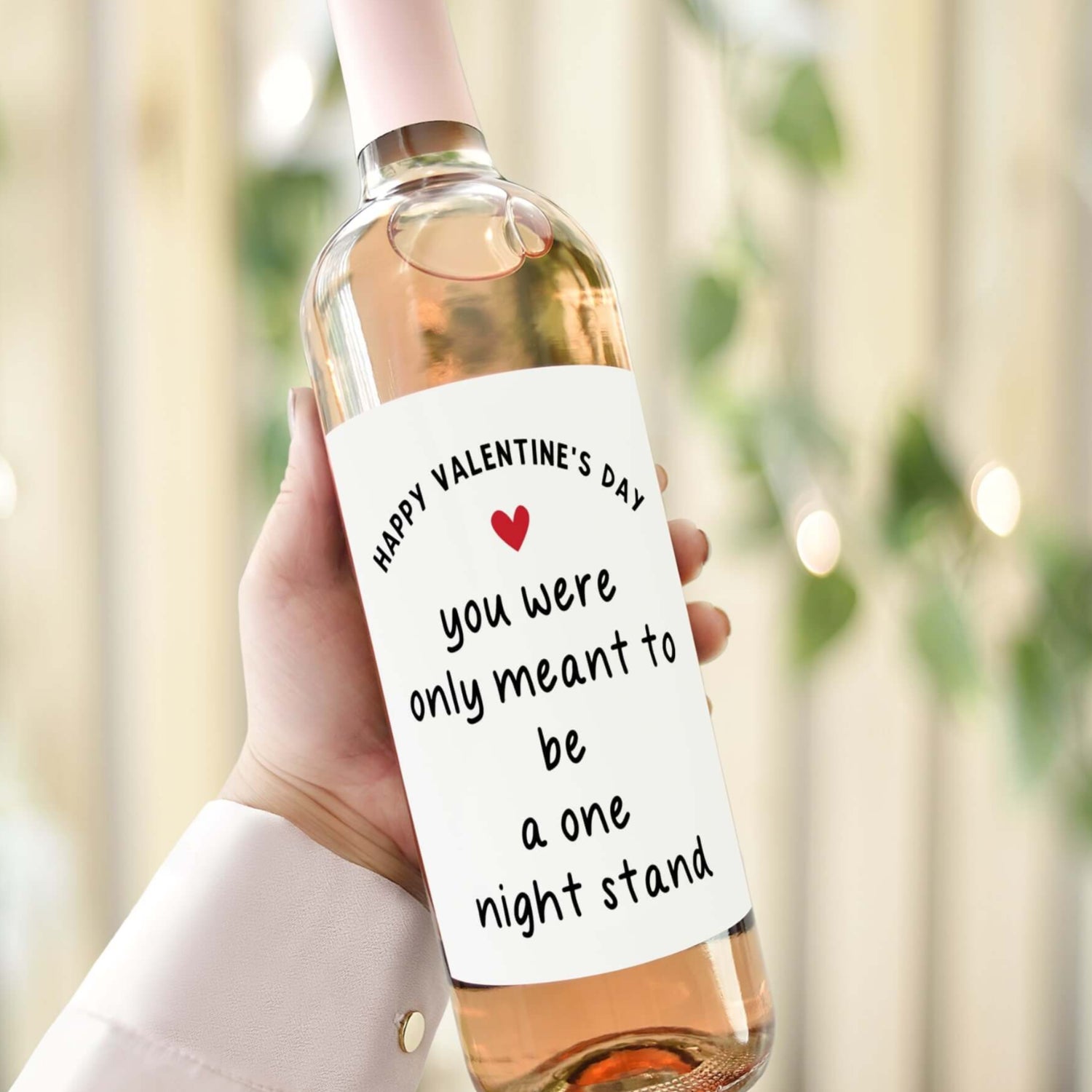 A hand holding a wine bottle with a cheeky Valentine’s Day label reading "You were only meant to be a one night stand.