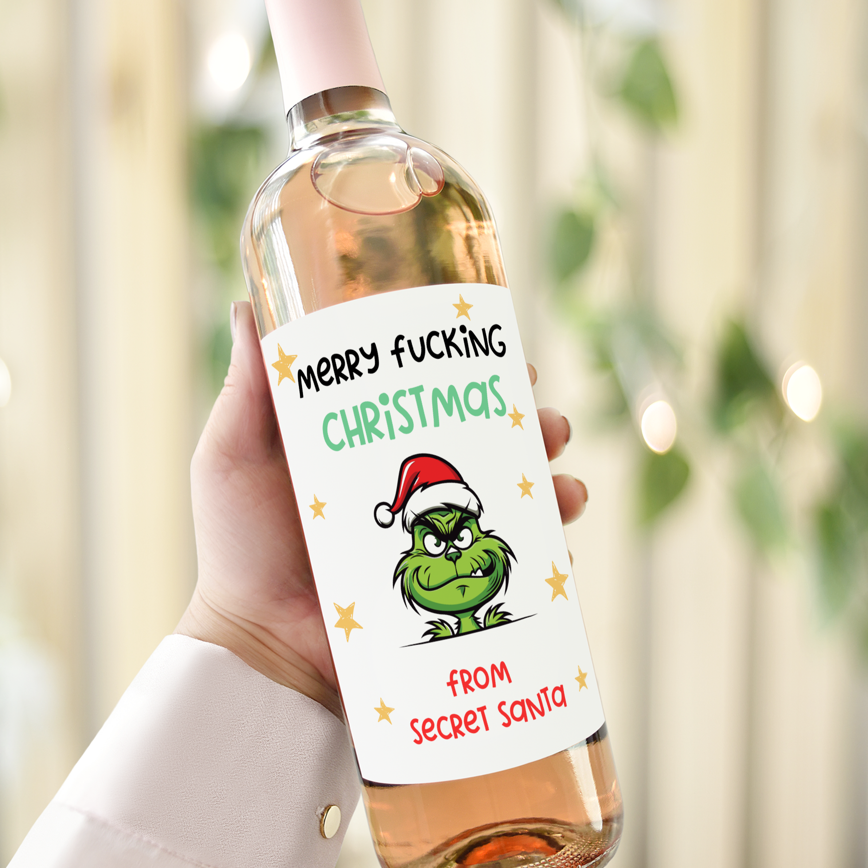 Wine bottle with a humorous Christmas label saying 'Merry F*cking Christmas from Secret Santa,' featuring a grumpy green character in a Santa hat.