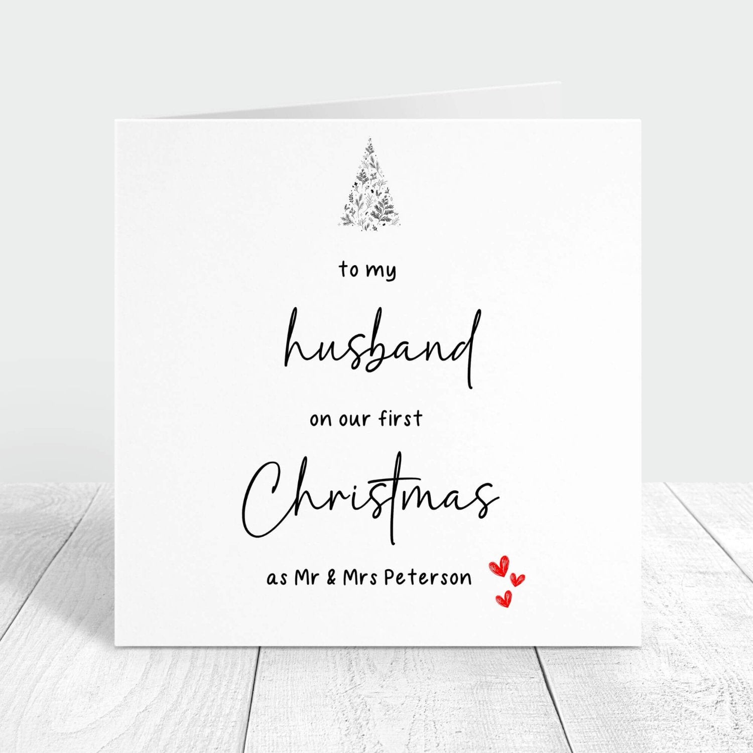 Personalised Christmas card for a husband featuring the message "To my husband on our first Christmas as Mr & Mrs Peterson" with festive accents like a Christmas tree and red hearts.