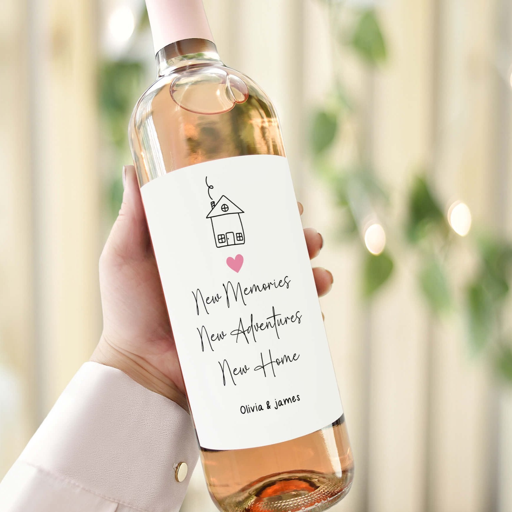 Hand holding a wine bottle with a personalised "New Home" label featuring a house illustration and the text "New Memories, New Adventures, New Home."