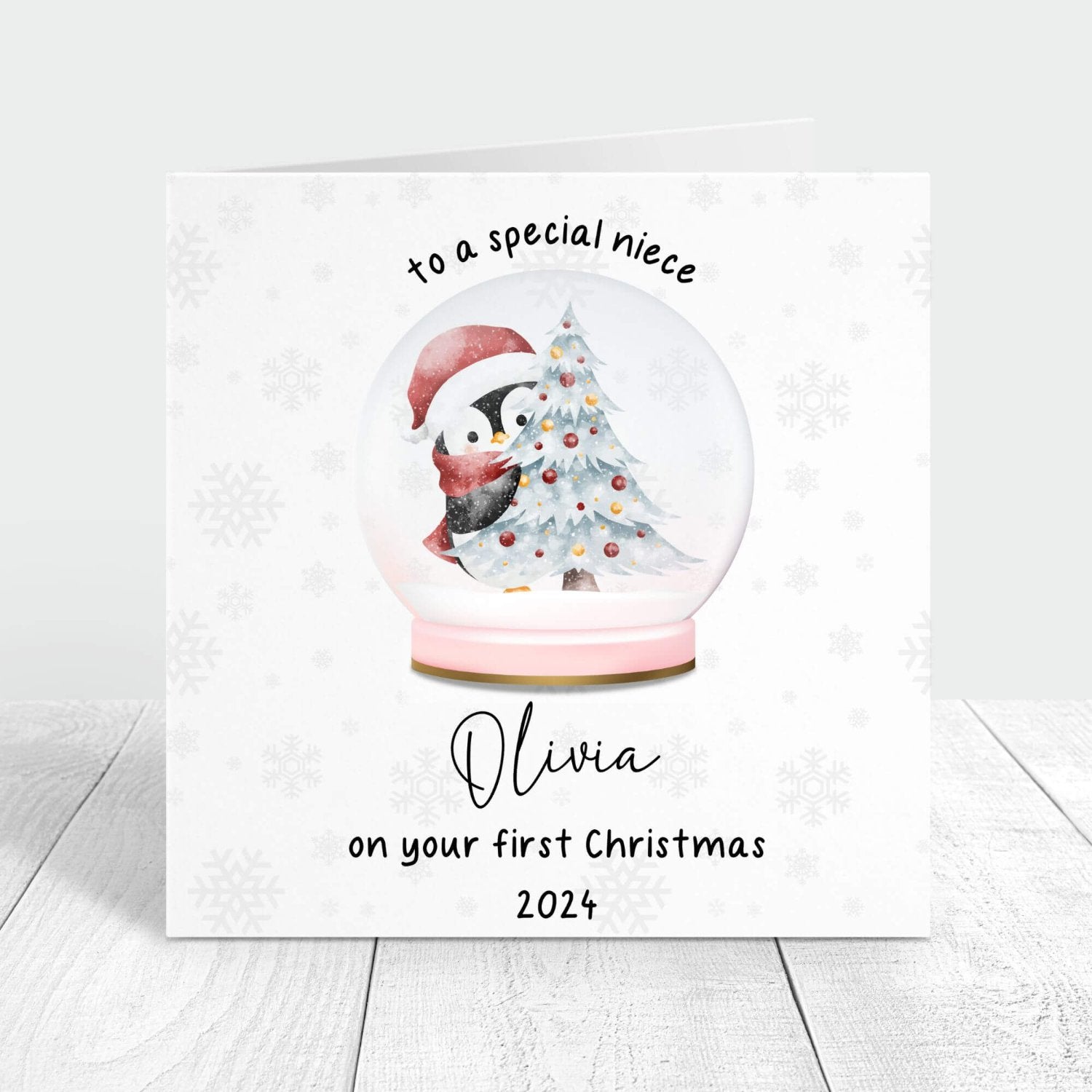 Personalised first Christmas card for niece featuring a snow globe with a penguin and Christmas tree, customised with her name and the year 2024.