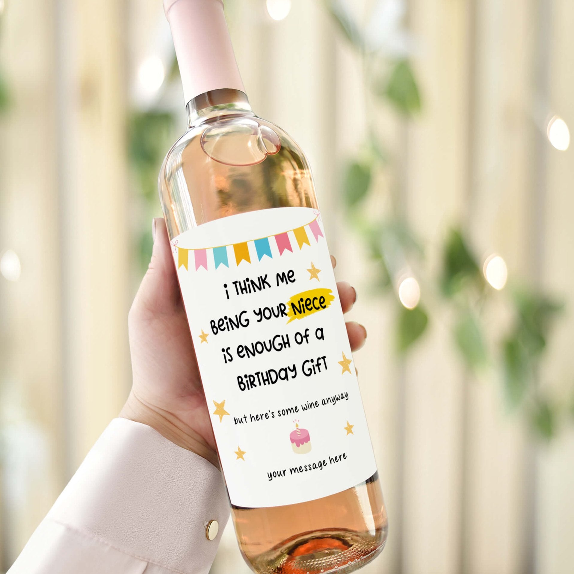 Wine bottle with a birthday label reading 'I think me being your niece is enough of a birthday gift,' displayed with macarons and champagne glasses.