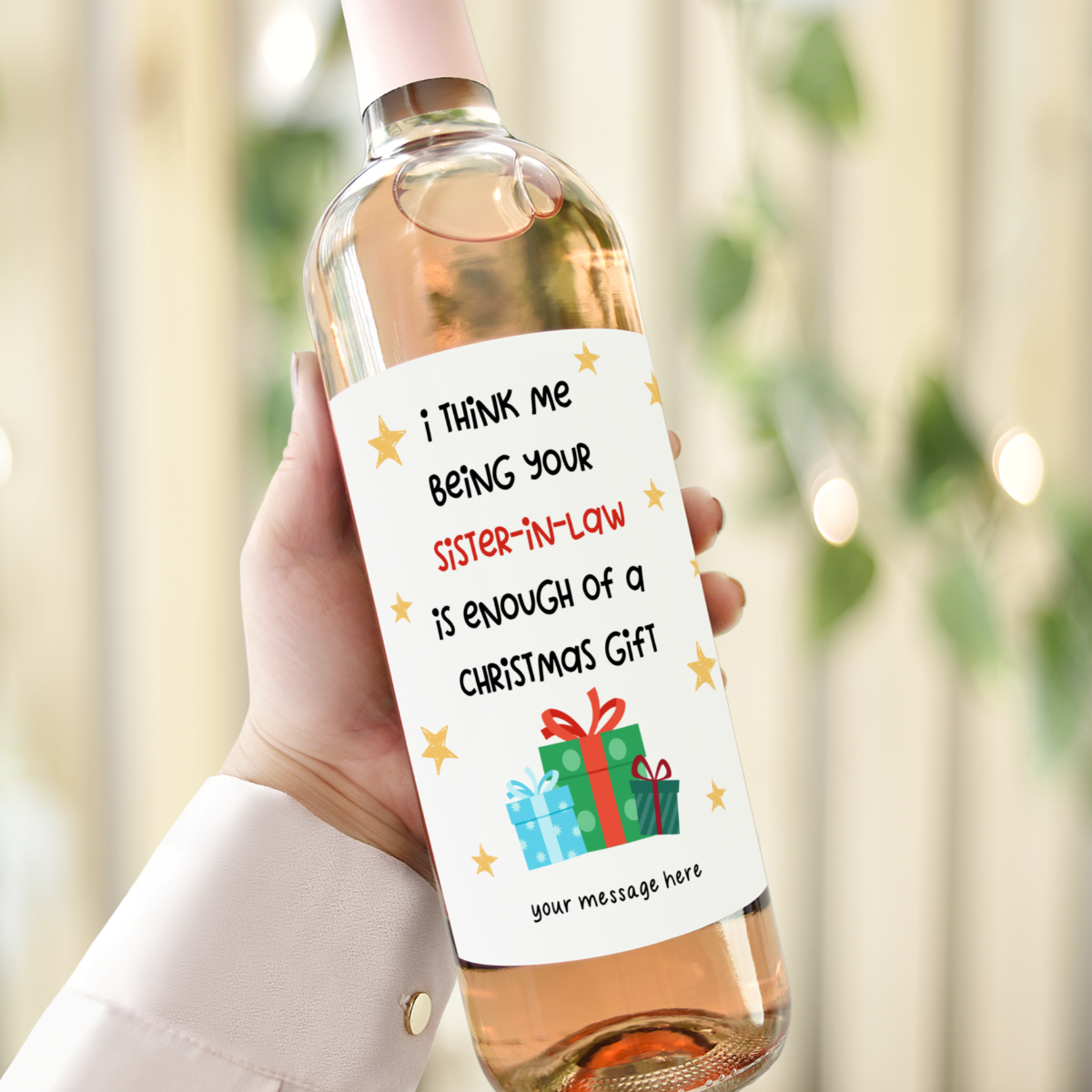 Hand holding a wine bottle with a humorous Christmas label for a sister-in-law, featuring stars and a festive gift graphic.