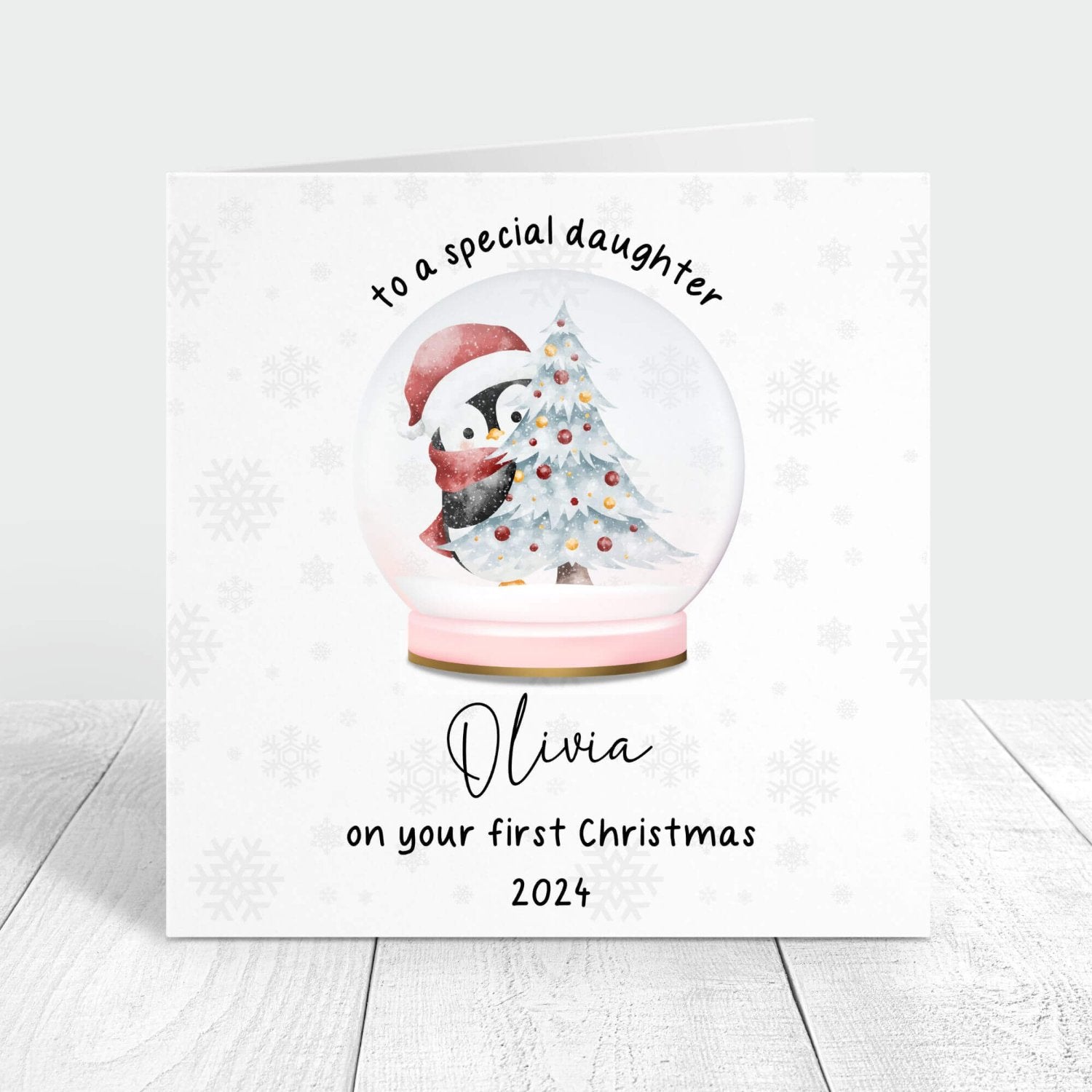 Personalised first Christmas card for daughter featuring a snow globe with a penguin and Christmas tree, customised with her name and the year 2024.